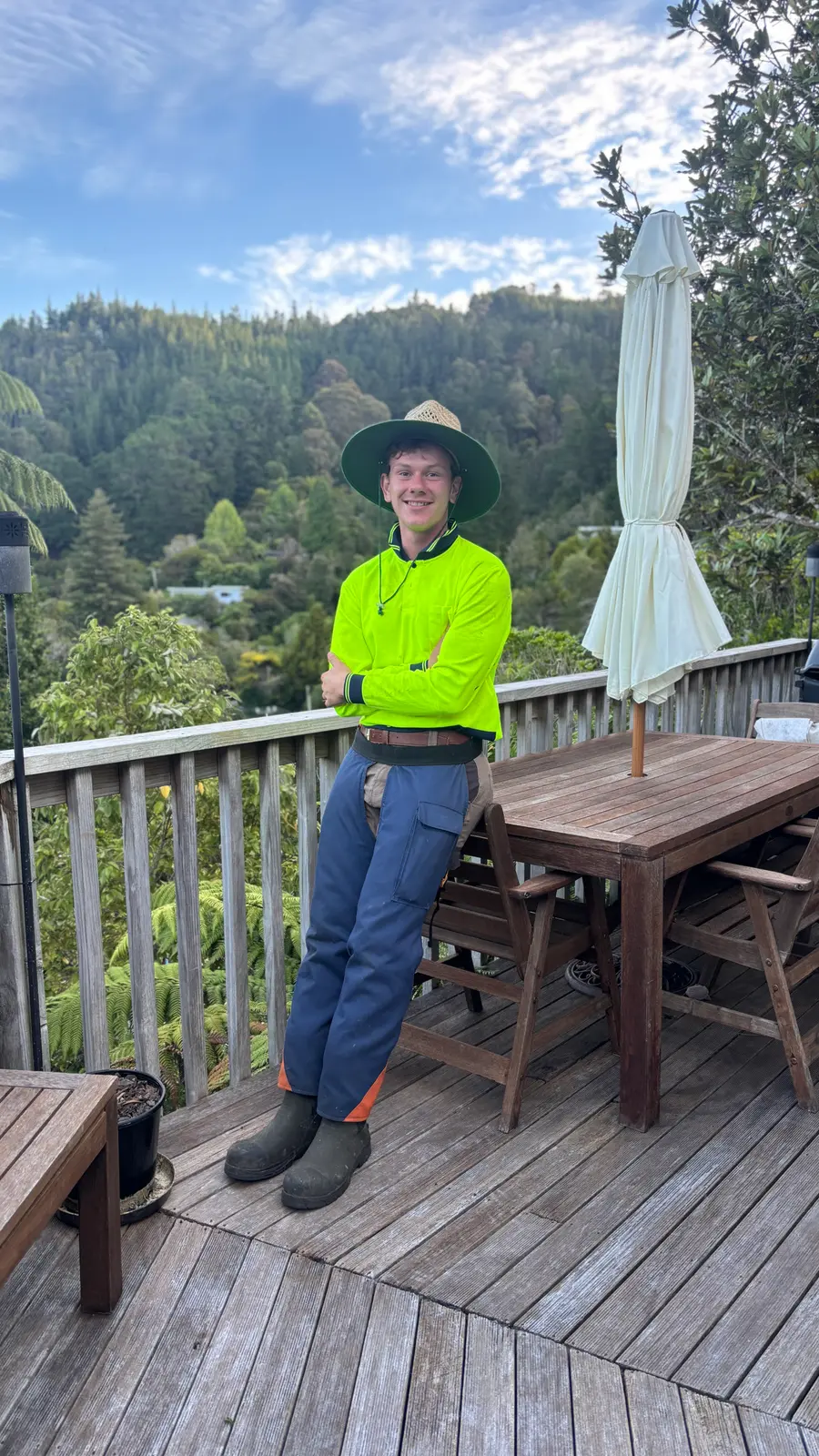 Johnny Batten in hi-vis with arms folded on a timber deck, bush-covered hills behind